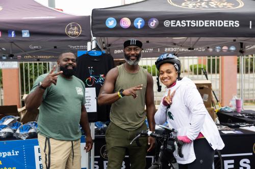 Three people smiling, posing at a bike event with tents in the background.